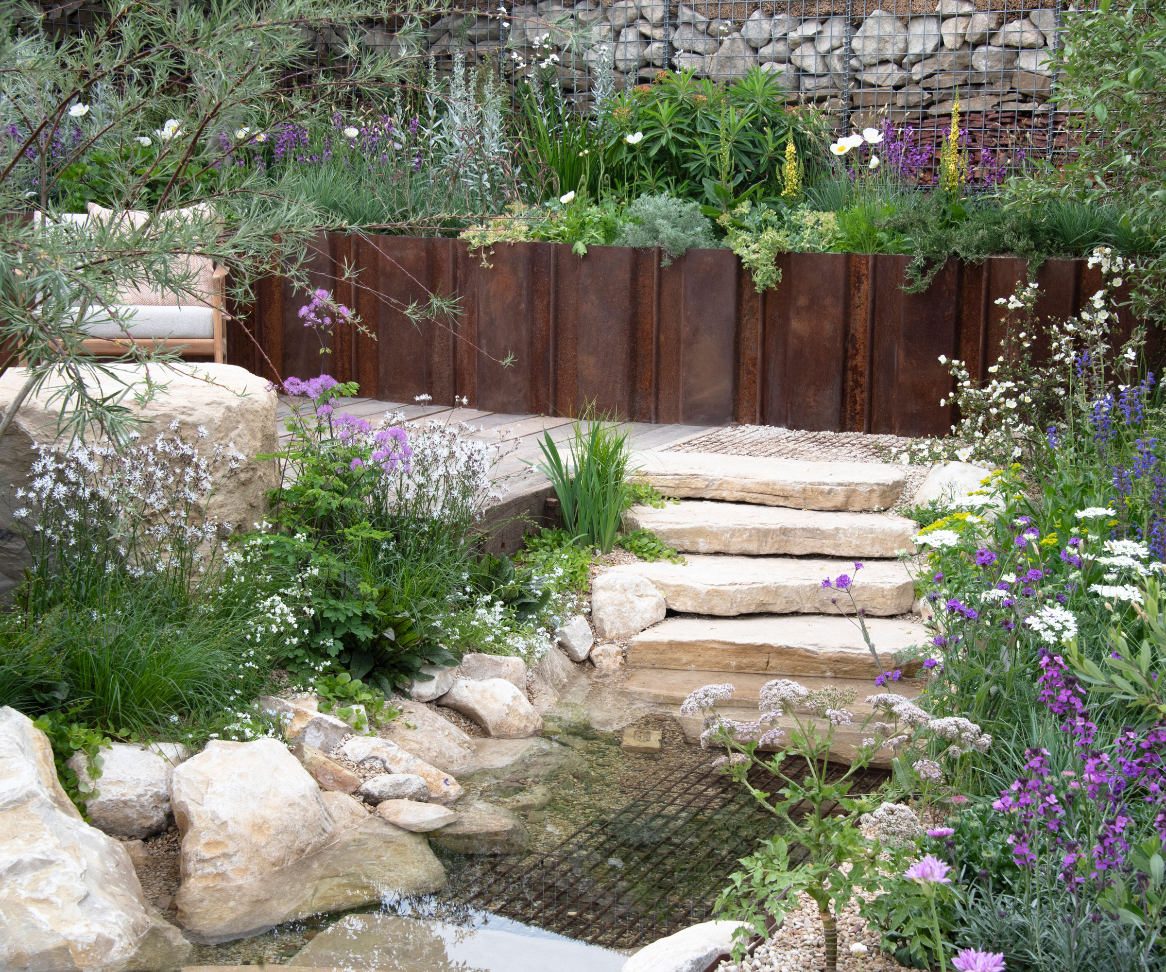 naturalistic garden design with unstructured planting, small garden pool, garden steps, rocks and chair