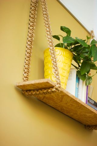 Shelf with woven hanger and yellow plant pot against yellow wall