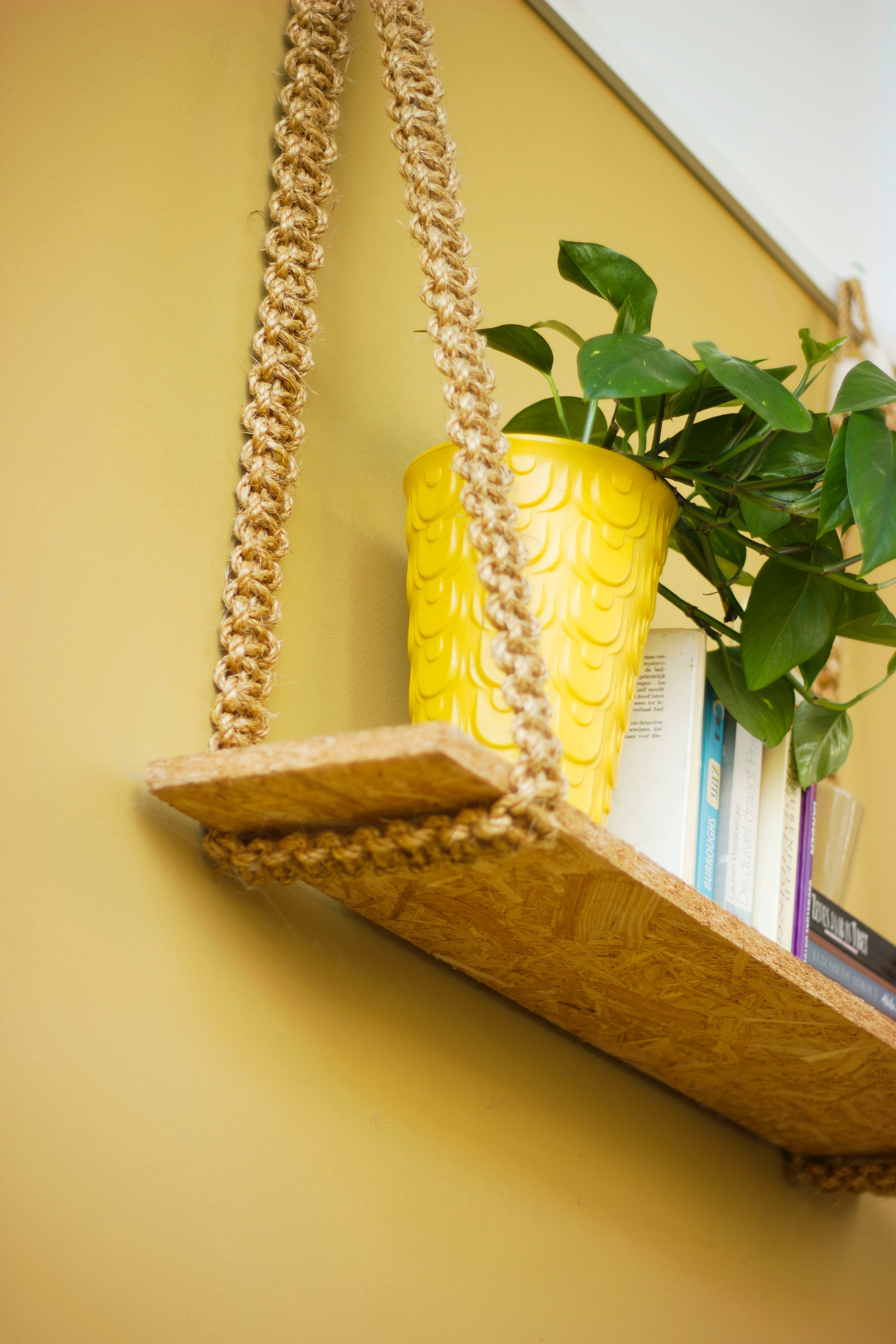 Shelf with woven hanger and yellow plant pot against yellow wall