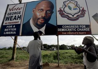 Liberians look at a campaign billboard for former footballer and presidential candidate George Weah in 2005.