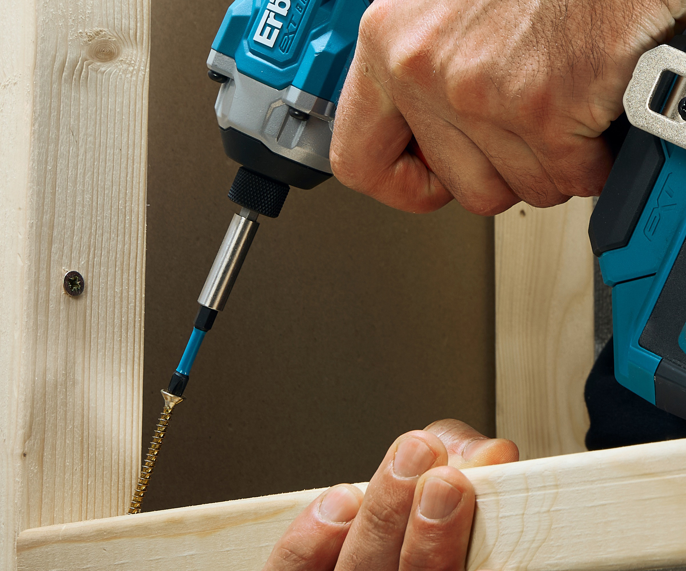 Close up of blue impact driver driving brass screw into timber frame