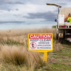 A sign warning about herbicide on the edge of a field with a truck in the background 