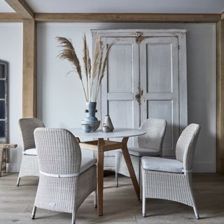 neutral pale grey dining room with rattan chairs, round table, armoire, vases on table, wooden floor boards