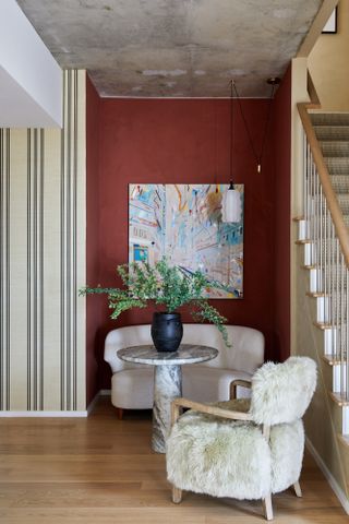 Entryway with beige and red walls, high-pile armchair and marble side table