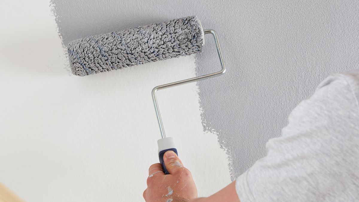 hand using roller to paint grey paint on white wall