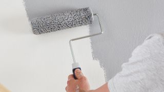 hand using roller to paint grey paint on white wall