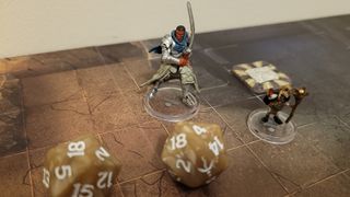 A model of a warrior wielding a sword stands in front of two dice and on a board from Dungeons & Dragons: Onslaught