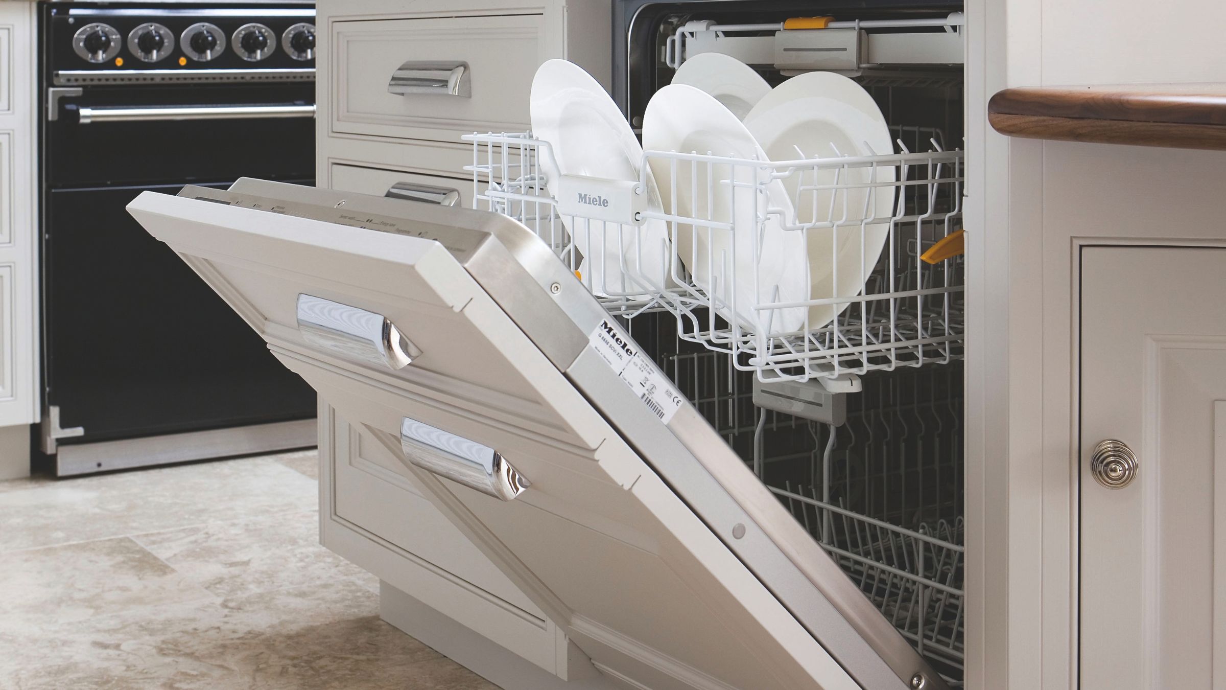 Open integrated dishwasher with plates inside, and cream cabinet on the front