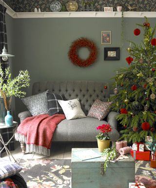 Green country living room with red Christmas decorations, a red wreath on the walls, and a grey sofa with cushions and a red throw