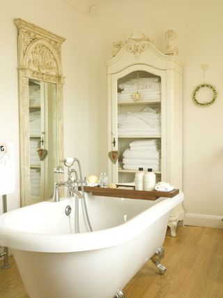 Bathroom with roll top bath, decorative mirror, and closet with linens with wood floor and neutral walls