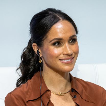 Meghan Markle wears her hair in a ponytail and wears a brown shirt