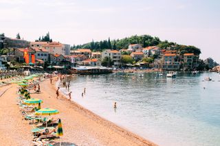 People sit under colorful umbrellas on a beach near Budva, Montenegro