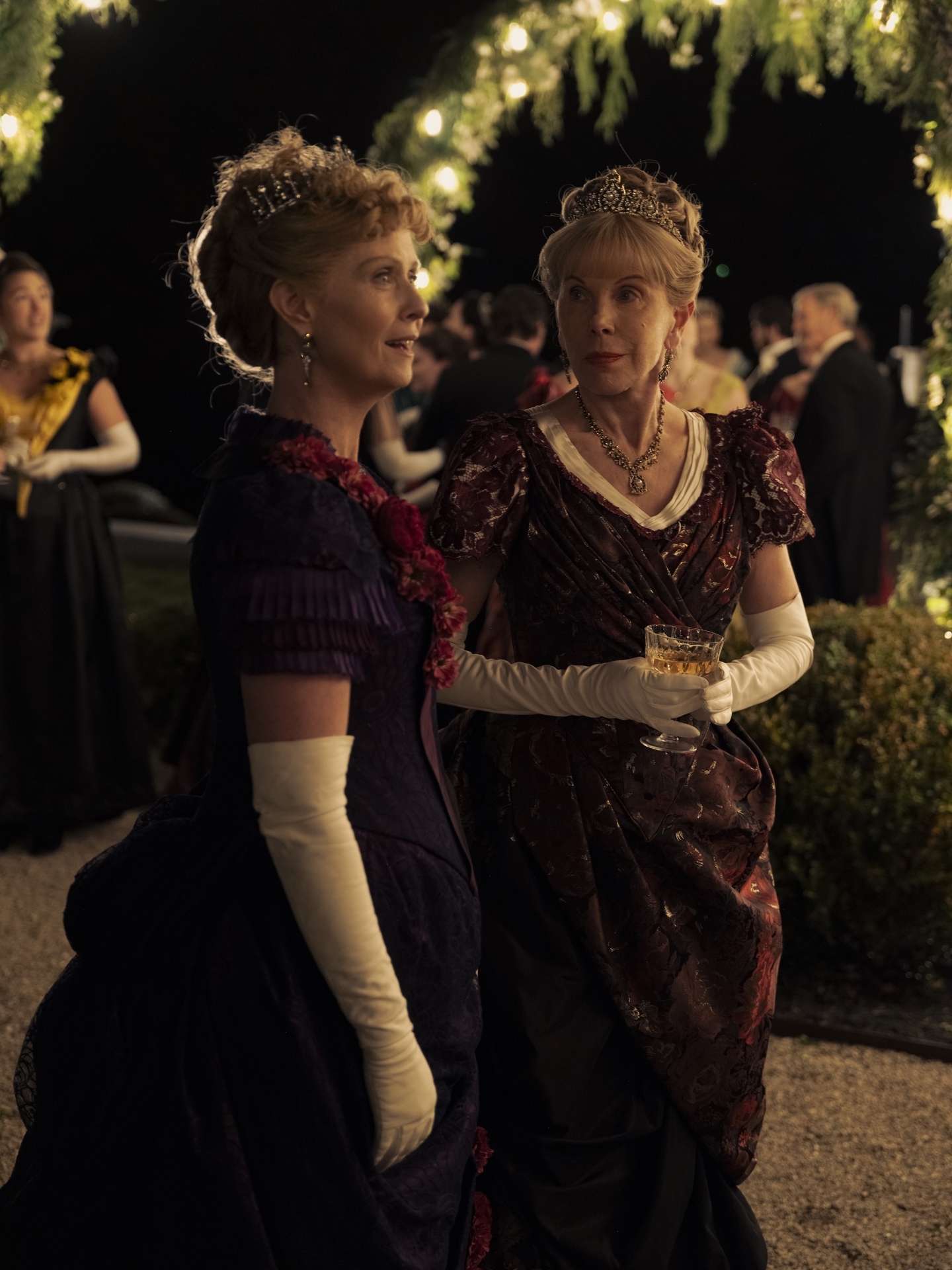 cynthia nixon and christine baranski wear maroon dresses and speak together at a high society event in the gilded age