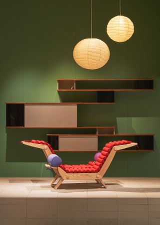 A green wall forms the backdrop for a hanging bookcase and a wooden chair with red cushions, both by Charlotte Perriand