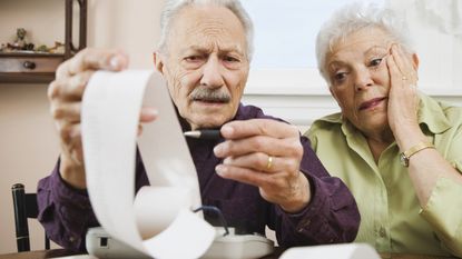 An older couple look nervous as they look at the tape from an old-fashioned calculator.