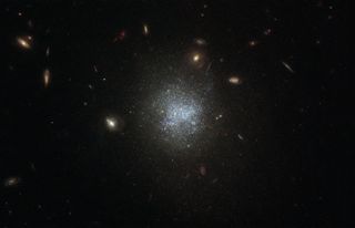 The faint galaxy UGC 695 shimmers in deep space in this view from the Hubble Space Telescope. Located 30 million light-years away within the constellation Cetus (The Sea Monster), UGC 695 is considered a low-surface-brightness galaxy, which means that it's even dimmer than the background brightness of Earth’s atmosphere, which makes it difficult to observe. While galaxies like this don't contain as many stars as their brighter counterparts, they are rich with dark matter.
