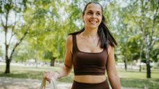 A woman in a park stands holding a resistance band, smiling.