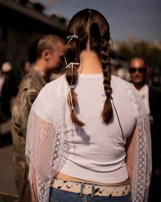 a woman at copenhagen fashion week wears two pigtail braids of different lengths with different accessories