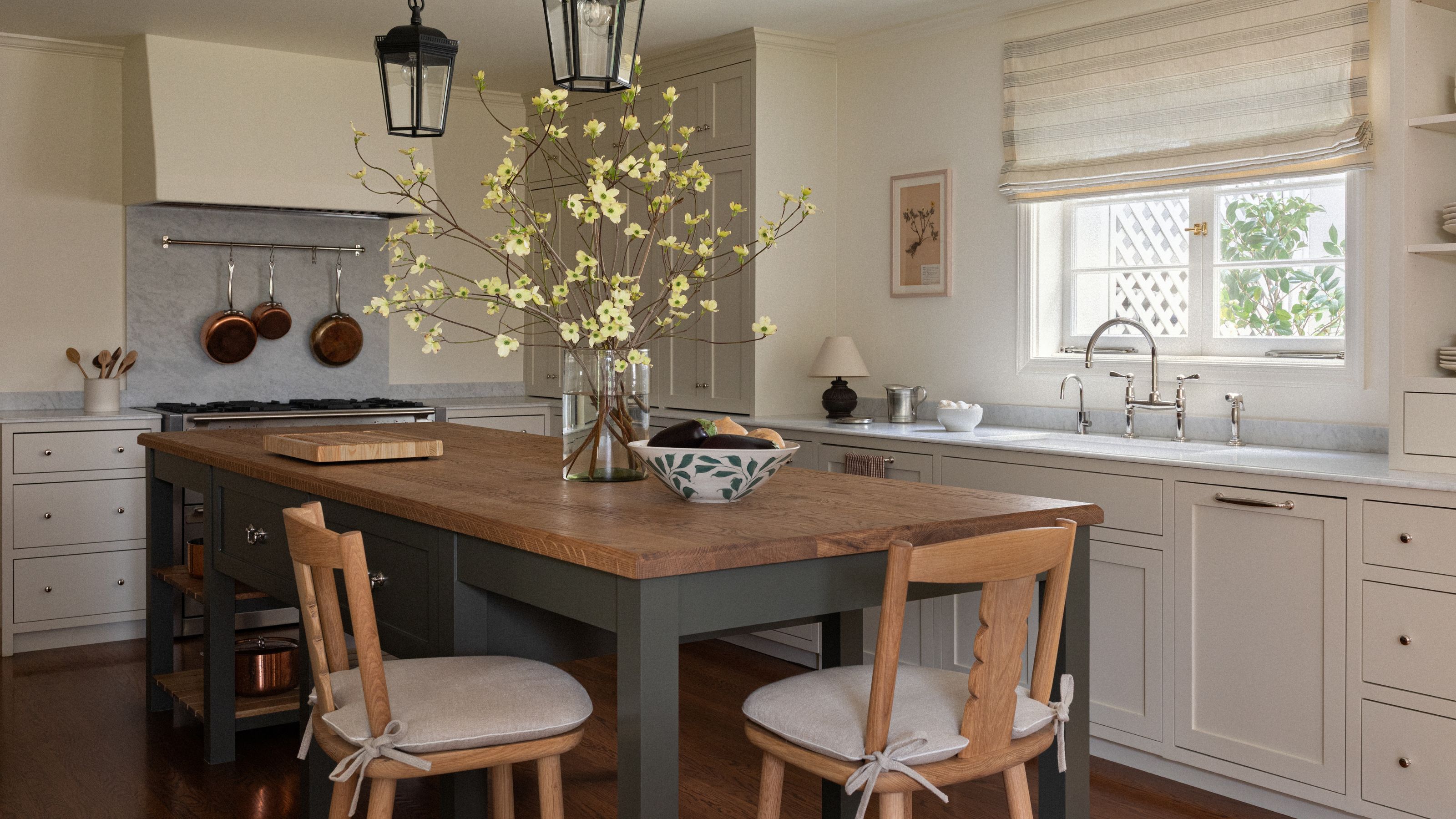 a soft neutral kitchen with marble countertops, a plaster cooker hood, and center island with bar stools