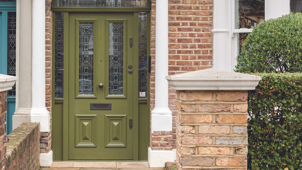 Olive green front door with four panels and a white pillar. 