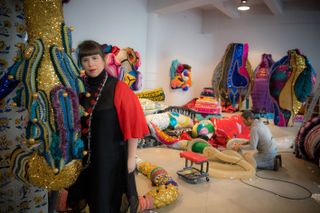 Pictured is Vasconelos in a black and red dress standign in a studio with various sea creatures in multiple colours.