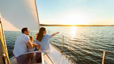 Family Of Three Sailing On Yacht Sitting On Sailboat Deck Looking At Sunset