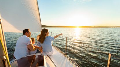Family Of Three Sailing On Yacht Sitting On Sailboat Deck Looking At Sunset