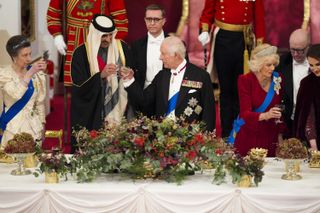 Queen Camilla, Princess Anne, and King Charles standing up and toasting the Amir and Sheika of Qatar at a white tie banquet