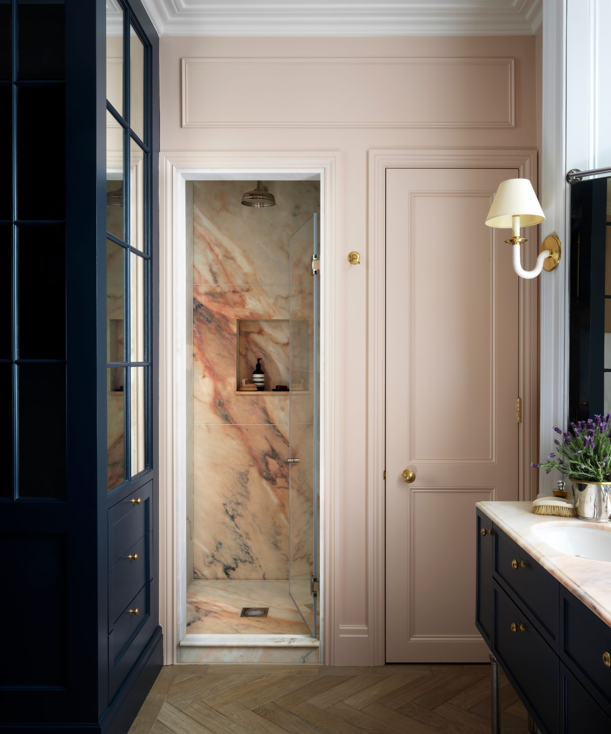 Bathroom with plaster pink cabinets, marble shower, navy blue painted vanity unit and sconce