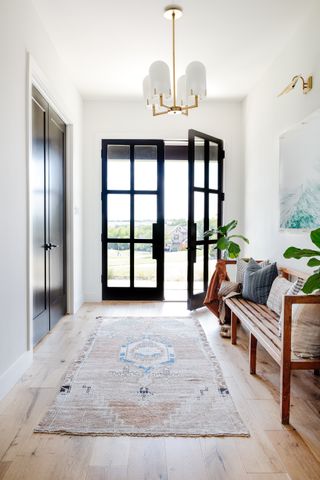 Entryway with open doors, bench and patterned rug.