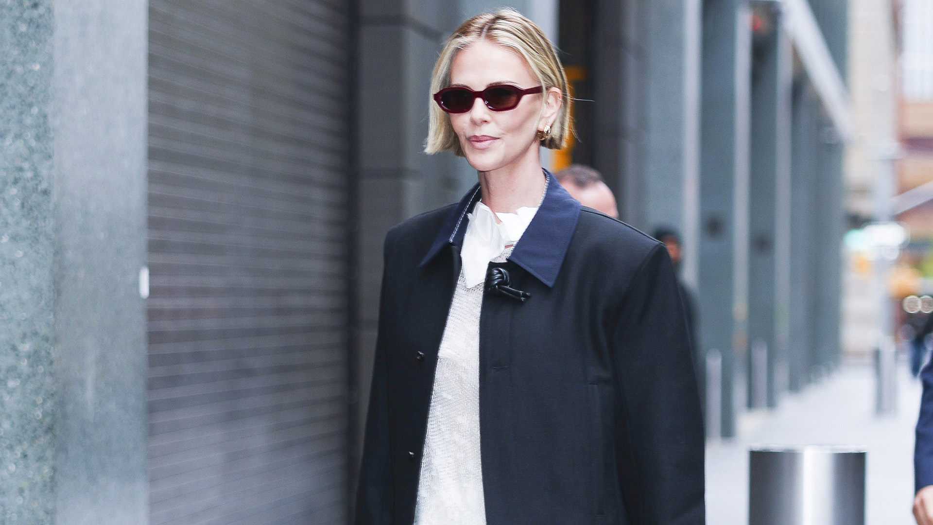Charlize Theron wearing a black coat over a white top and skirt with soft oxford flats in white leather