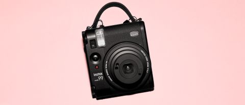 A photograph of the Fujifilm Instax mini 99 in black, set against a pink background.