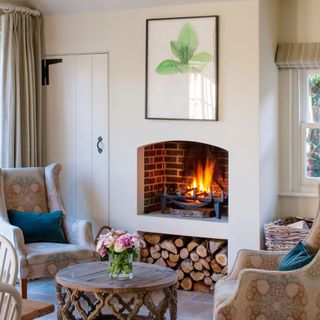 open fire in fireplace with log store underneath flanked by armchairs and coffee table future
