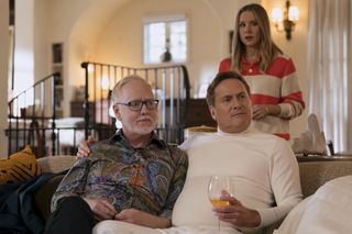 Two men (Patrick Bristow as Pat and Michael Hitchcock as Henry) sit on a couch as a woman (Kristen Bell as Joanne) stands behind them in a living room, in episode 104 of Nobody Wants This.