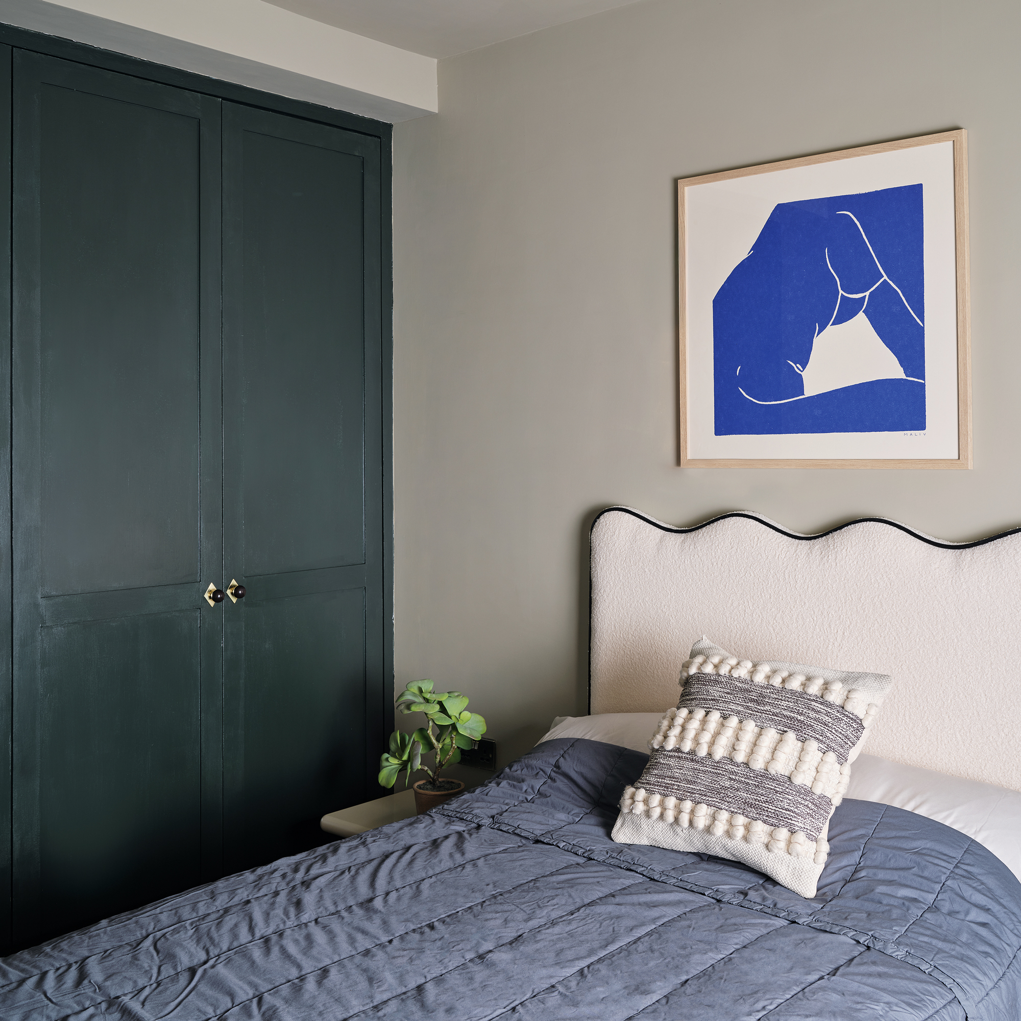 a small bedroom with dark green painted fitted wardrobes, a white upholstered headboard and a blue bedspread