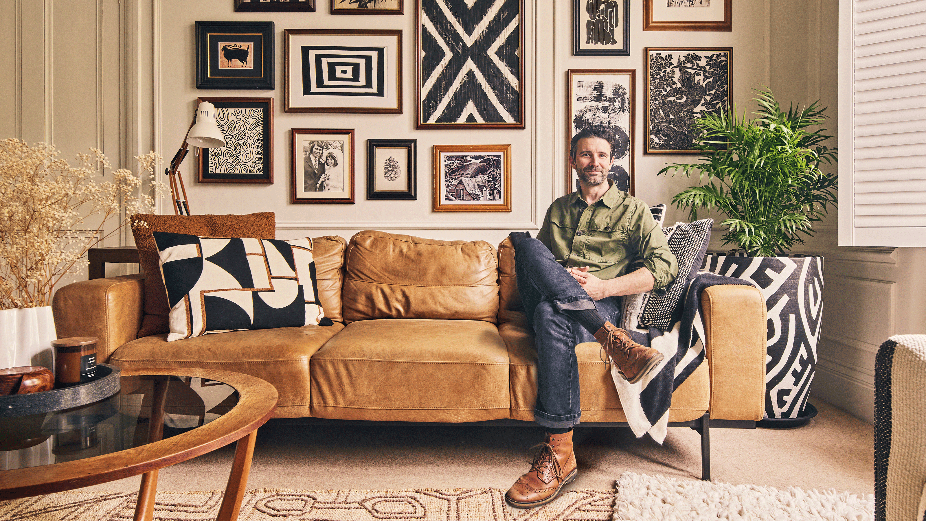 Interior designer John Cooper sitting on a brown leather sofa in is living room with a bold gallery wall behind him