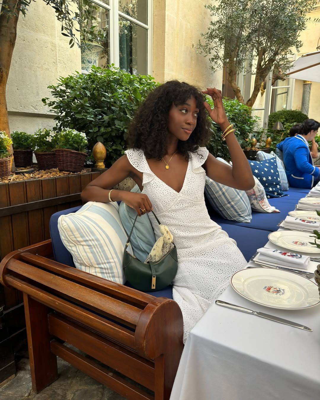 @emmanuellek_ wears a white broderie dress with ruffle sleeves while she sits at a Parisian restaurant