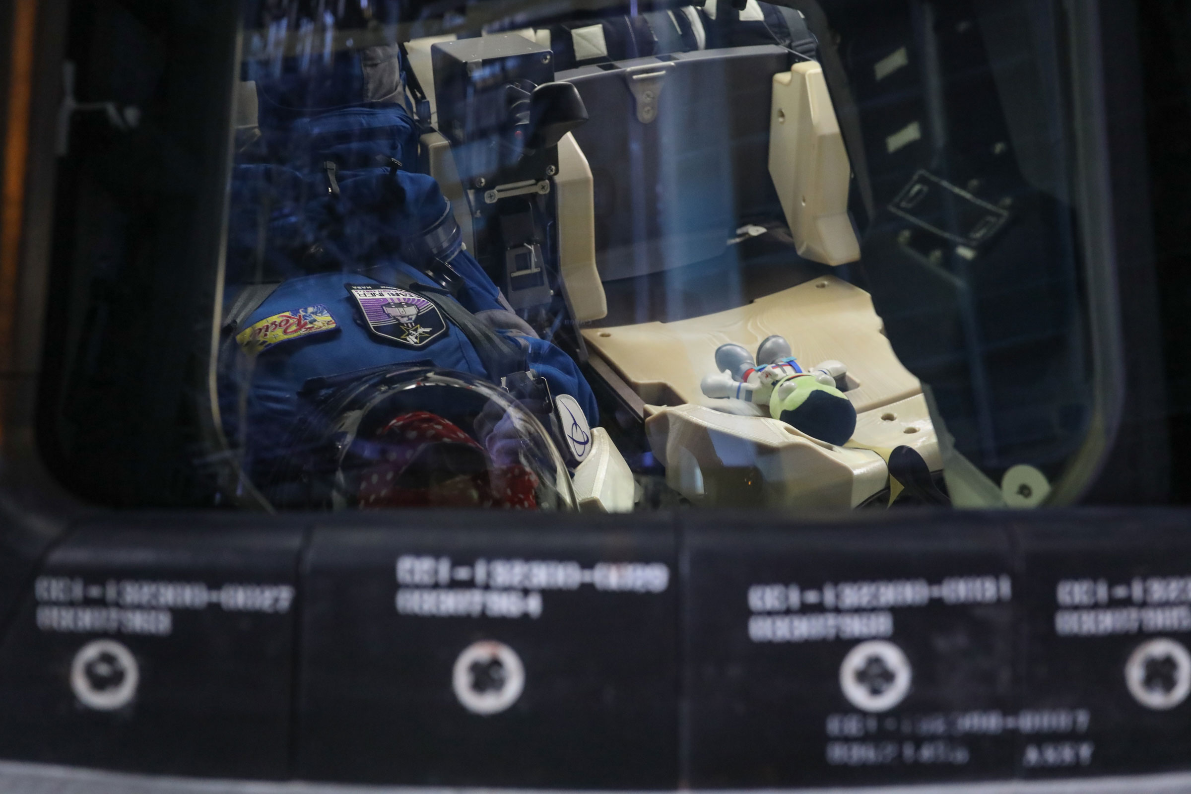 Boeing's Starliner Orbital Flight Test-2 zero-g indicator, a plush Jeb from the game Kerbal Space Program, is seen through a window into the space capsule. Jeb is seated next to "Rosie the Rocketeer," an anthropometric test device.