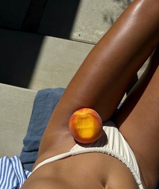 Pembuat konten berbaring di bawah sinar matahari dengan buah persik di pangkuannya