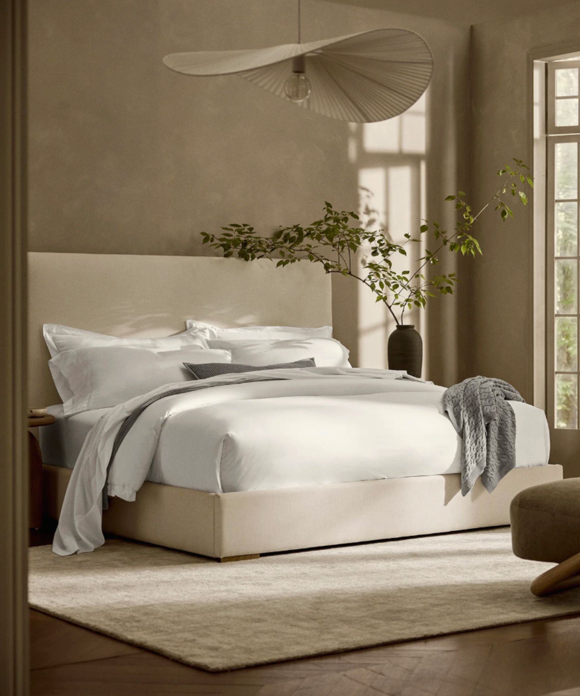 Minimalist bedroom with neutral fabric bedframe and white sheets on the bed