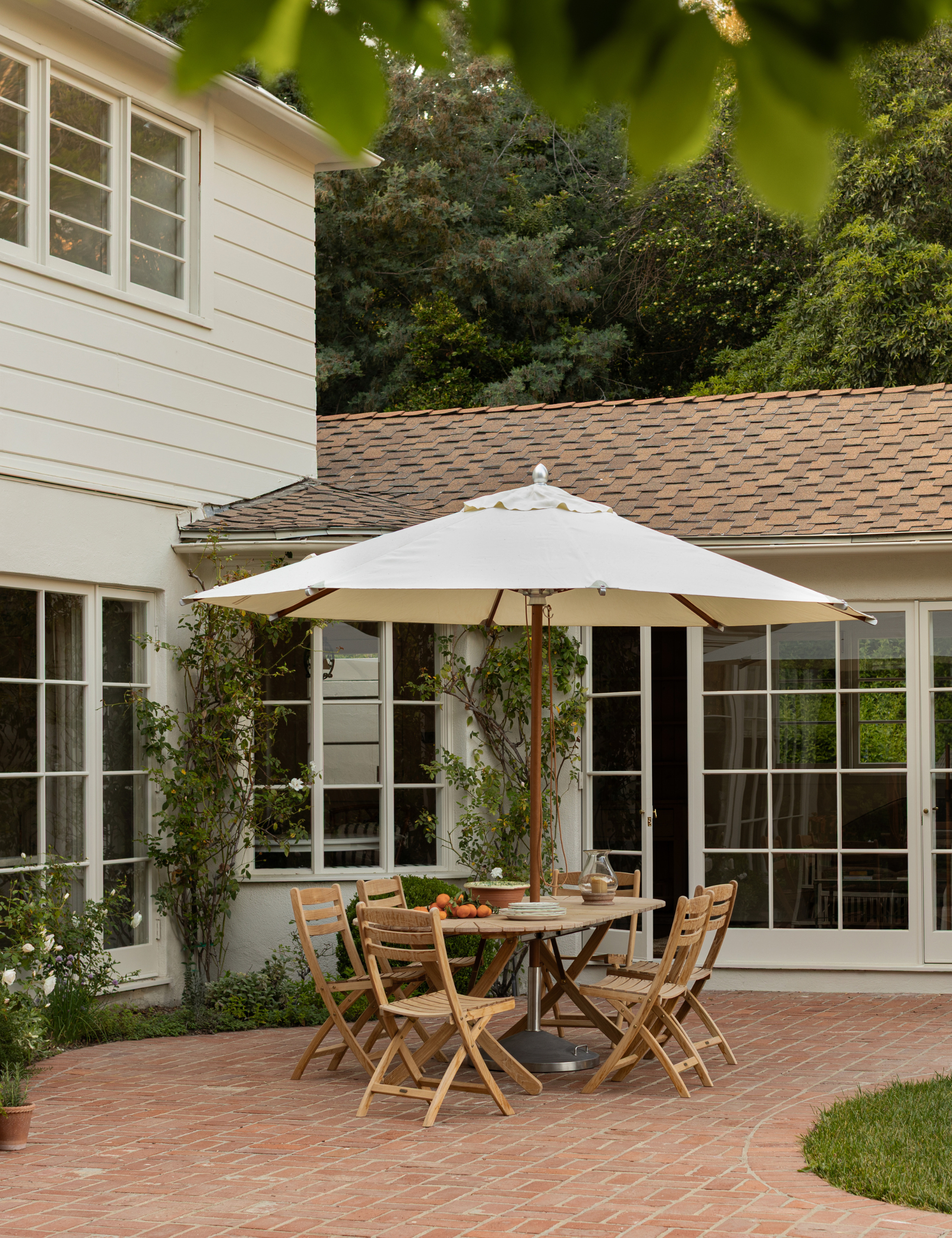 Brick patio area featuring crawling vines and a wooden dining table and chairs, shaded by a cream umbrella