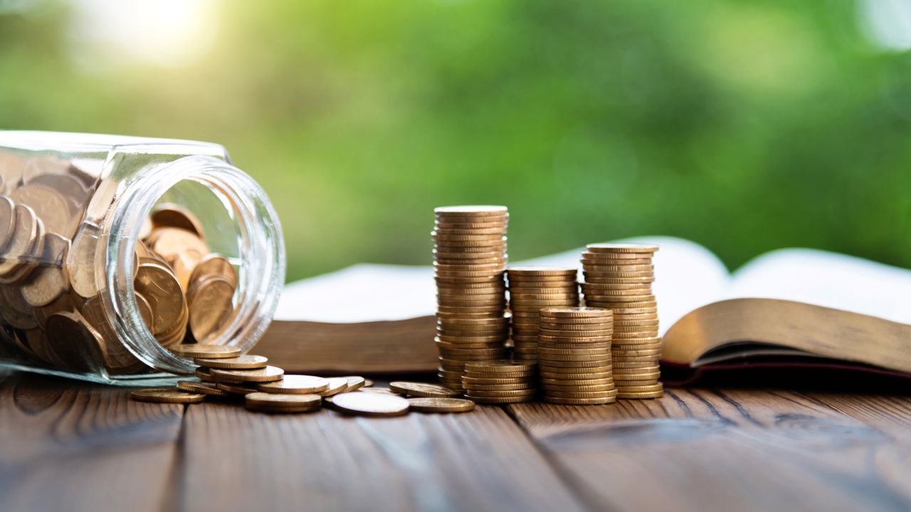 Coins in piles and in a jar, with an open book behind