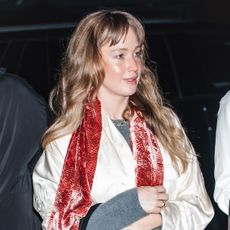 Jennifer Lawrence wearing a cream satin coat, jeans, flip-flops, and a pink velvet scarf