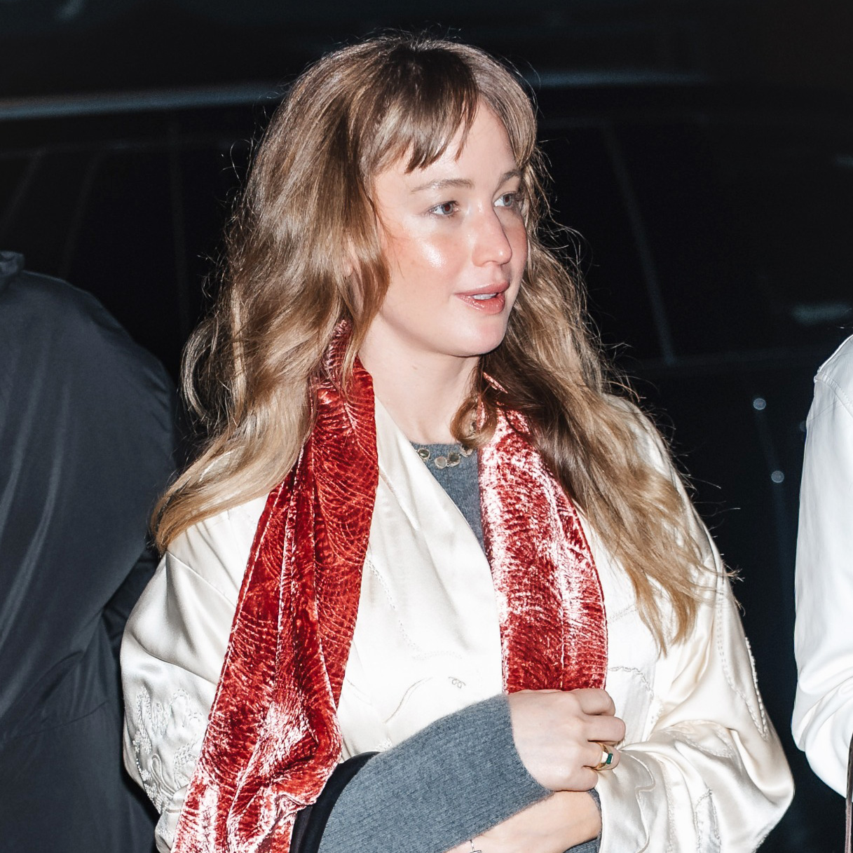Jennifer Lawrence wearing a cream satin coat, jeans, flip-flops, and a pink velvet scarf