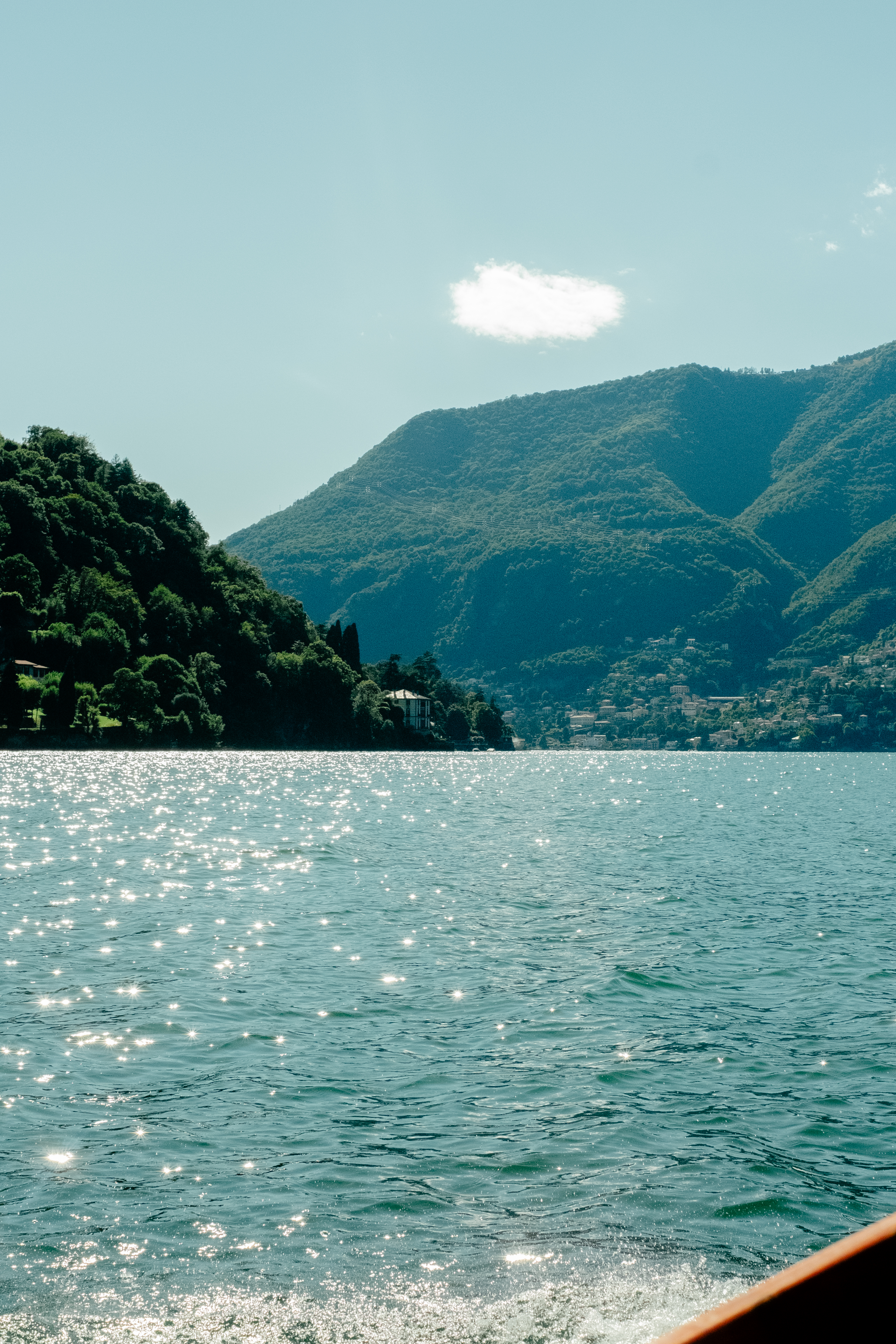 A lake alight with sunshine features verdant vegetation and hilly peaks.