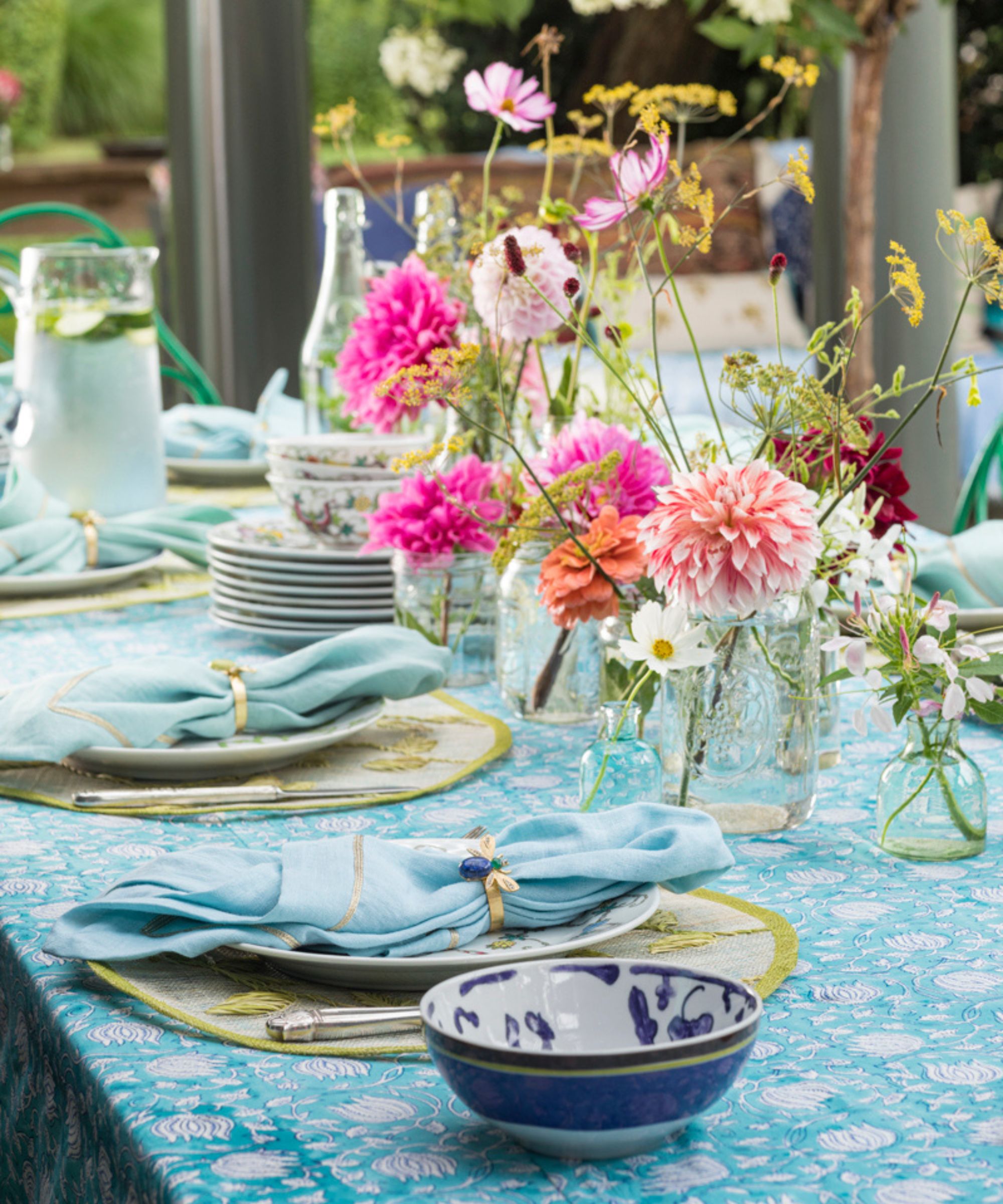 Table setting in light blues and greens with pink flowers in glass jars along the center