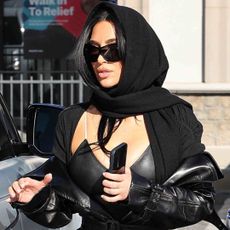 Kim Kardashian goes undercover in all-black attire, including the leather trench coat trend and a peekaboo bra