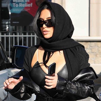 Kim Kardashian goes undercover in all-black attire, including the leather trench coat trend and a peekaboo bra