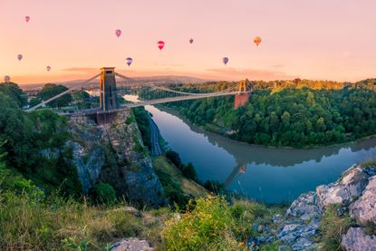 Many Hot Air Balloons drift towards Clifton Suspension Bridge in Bristol at sunrise. The bridge spans the River Avon gorge.