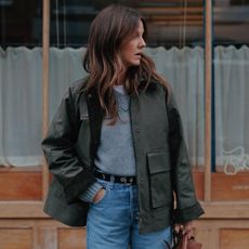 Woman wears green jacket, grey jumper, blue jeans